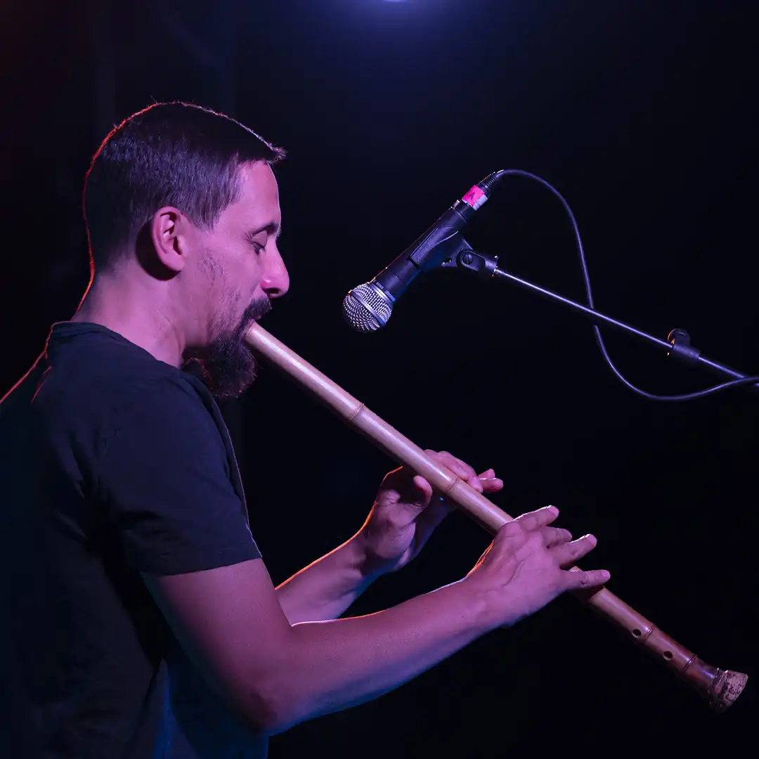 Man playing long wooden flute into a microphone, profile shot
