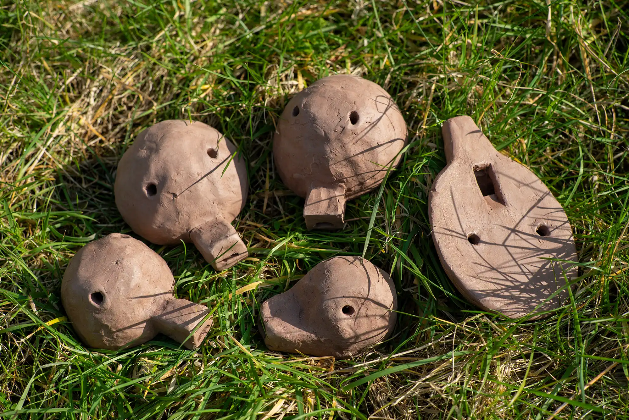 5 clay ocarinas placed onto some grass