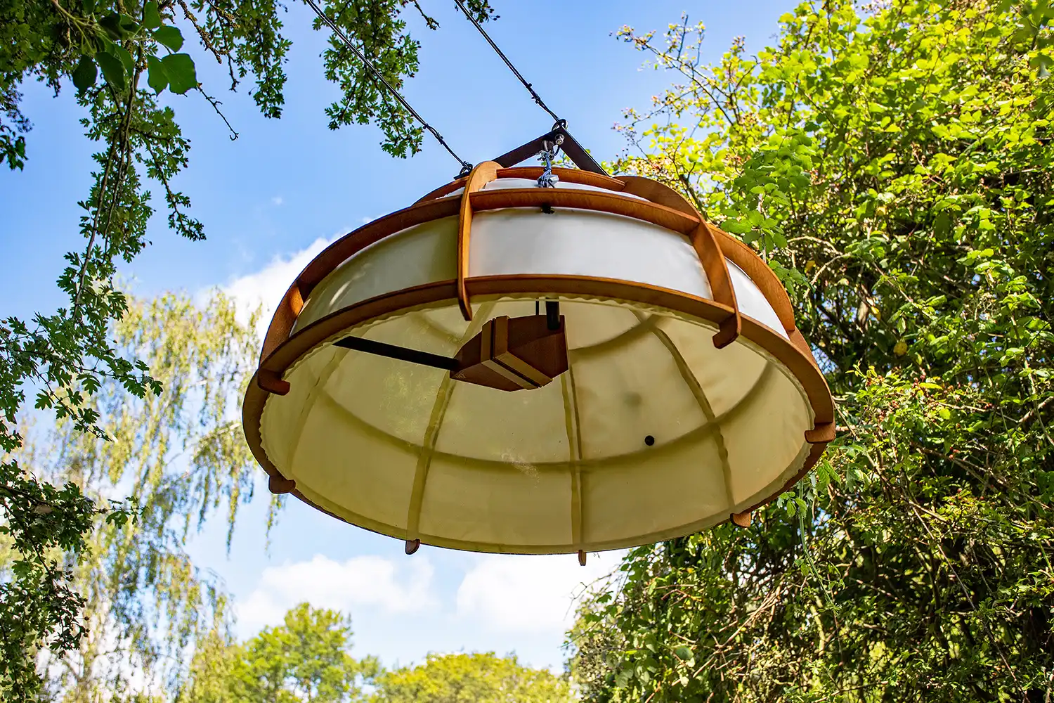 A canvas covered hemisphere with skeletal wooden frame suspended overhead in the tree canopy